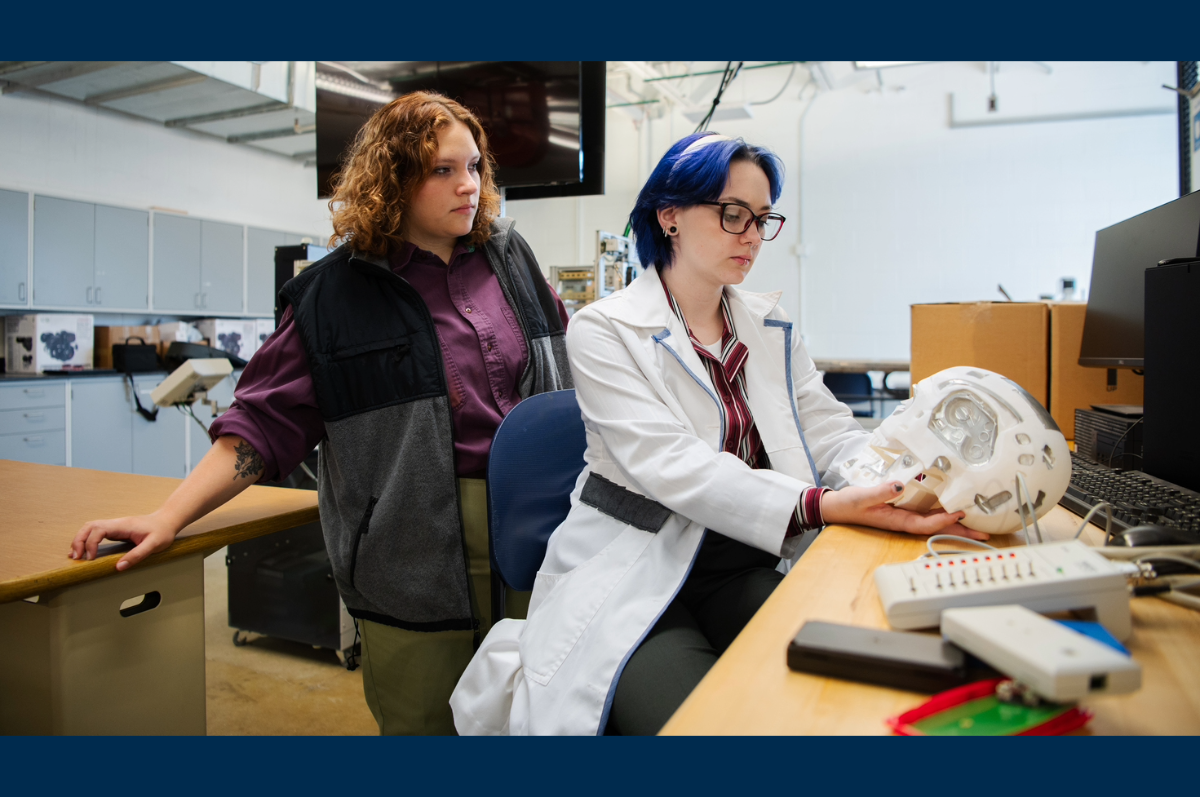 woman in purple shirt looks over woman in lab coat holding robot head